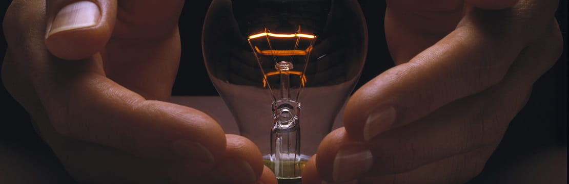 A pair of hands cups a softly glowing vintage lightbulb.