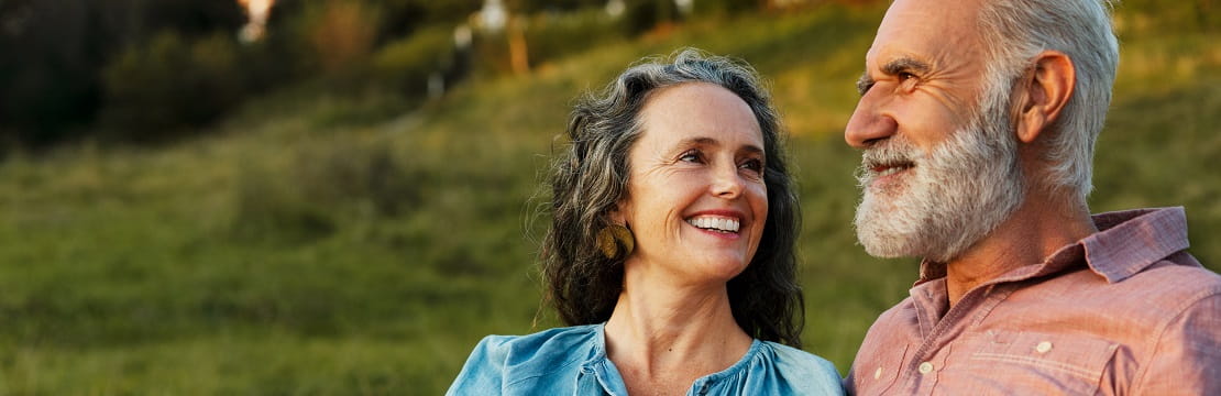 A mature, smiling couple seated beside one another outside